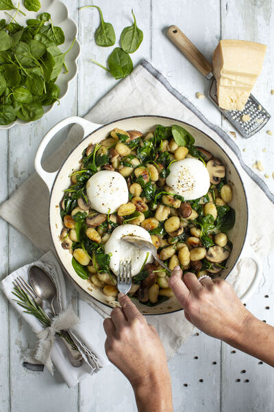 Gnocchi with spinach and mushrooms topped with burrata in a white pan, a fork lifting a portion