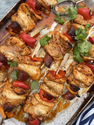 Chicken, chorizo and red pepper kebabs on wooden skewers in a roasting tray, scattered with coriander