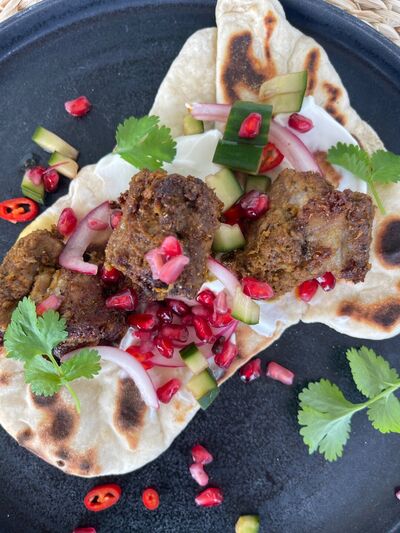 Indian spiced lamb kebabs on a charred flatbread with pickled cucumber, red onion, pomegranate seeds and coriander