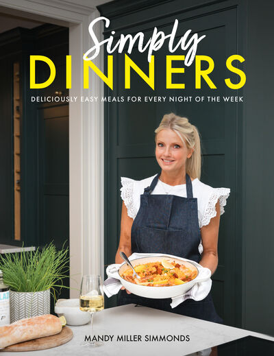 Front cover of Simply Dinners by Mandy Miller Simmonds: Mandy in a denim apron holding a dish in her dark green kitchen