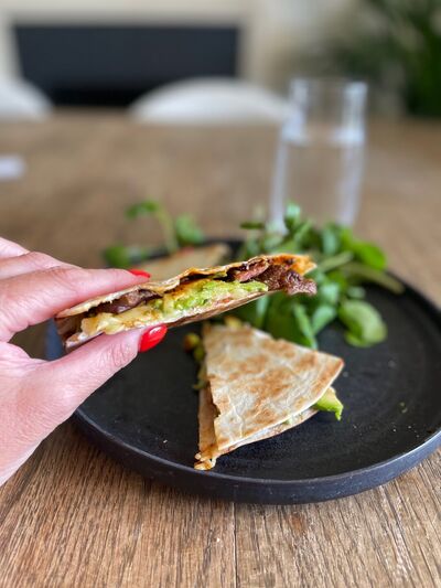 Leftover steak quesadilla cut into wedges on a dark plate, held in one hand